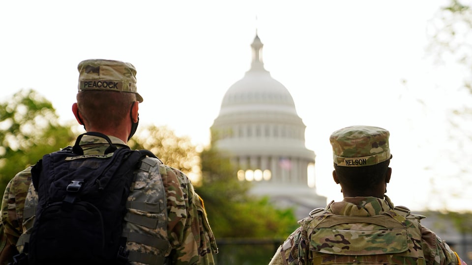 Two members of the National Guard, from behind, look at the Capitol.