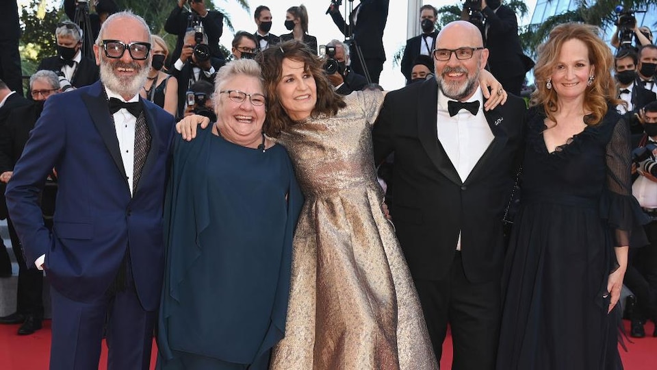 Three men and two women smiling on the red carpet. 